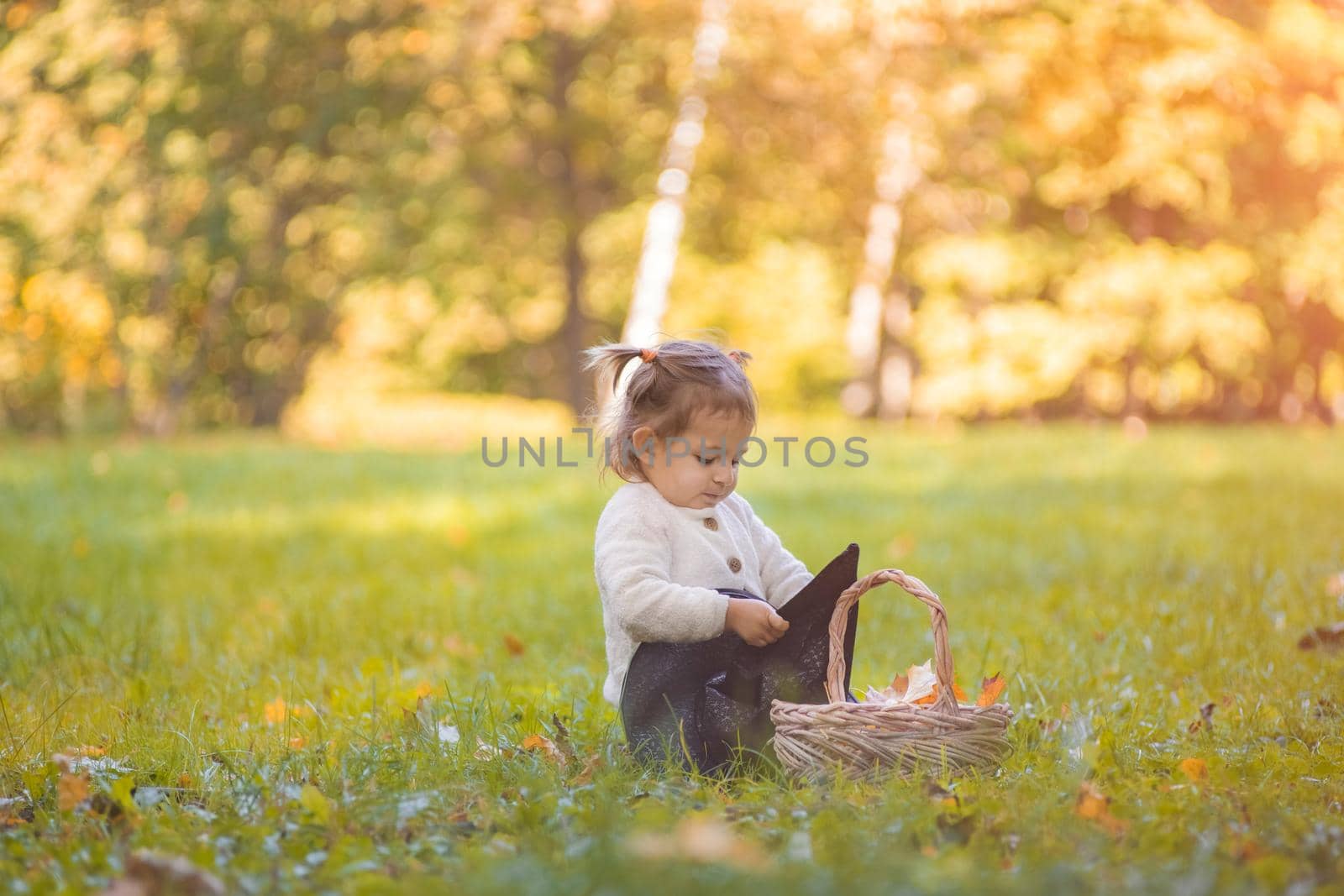 halloween celebration concept. cute toddler playing with witch hat on the lawn in the autumn park on a sunny day.