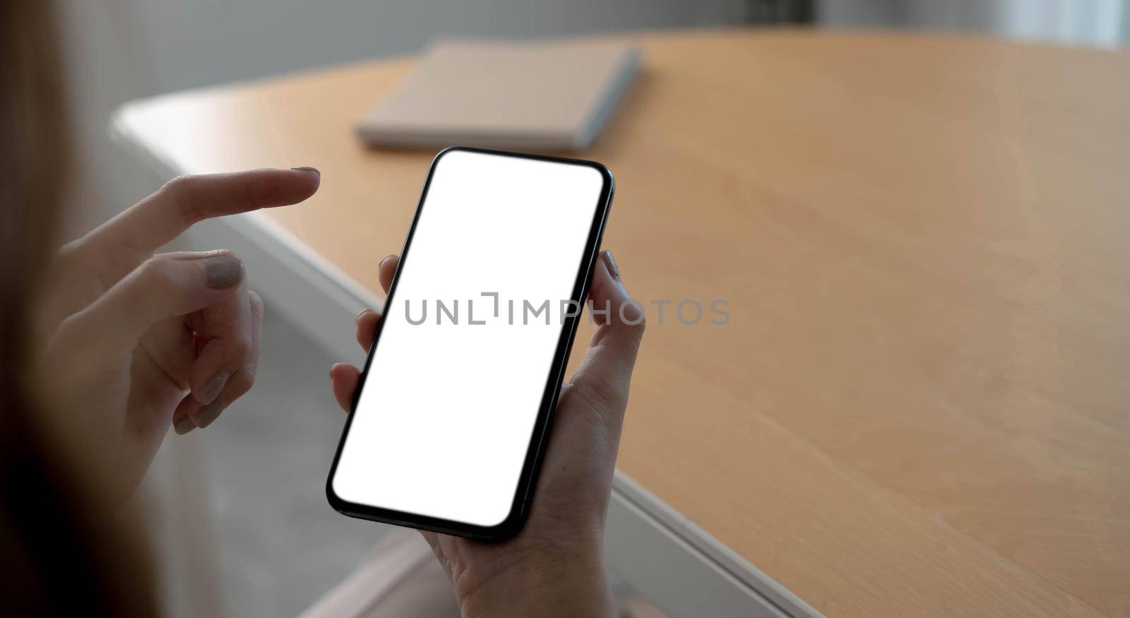 Mockup image blank white screen cell phone.women hand holding texting using mobile on desk at home office. by wichayada