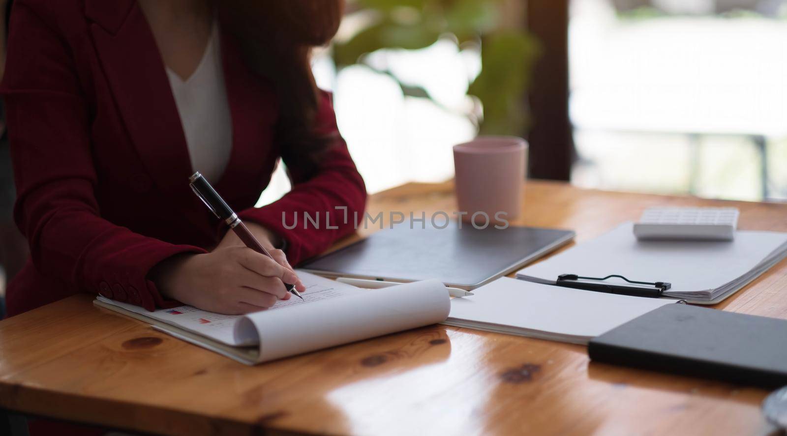 Female accounting or bookkeeper providing accounting service for small businesses, holding pen to make notes and using calculator, woman using digital tablet and calculator by wichayada