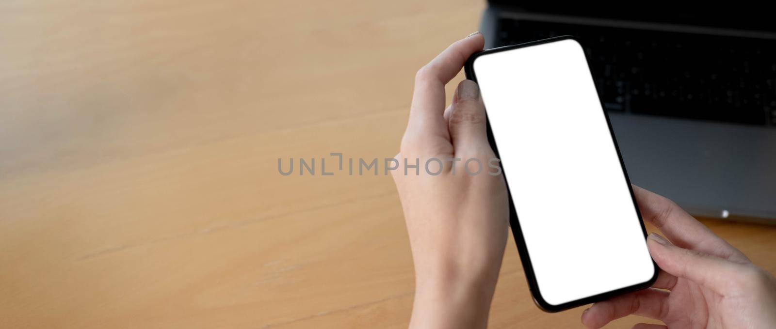 Mockup image blank white screen cell phone.women hand holding texting using mobile on desk at home office...