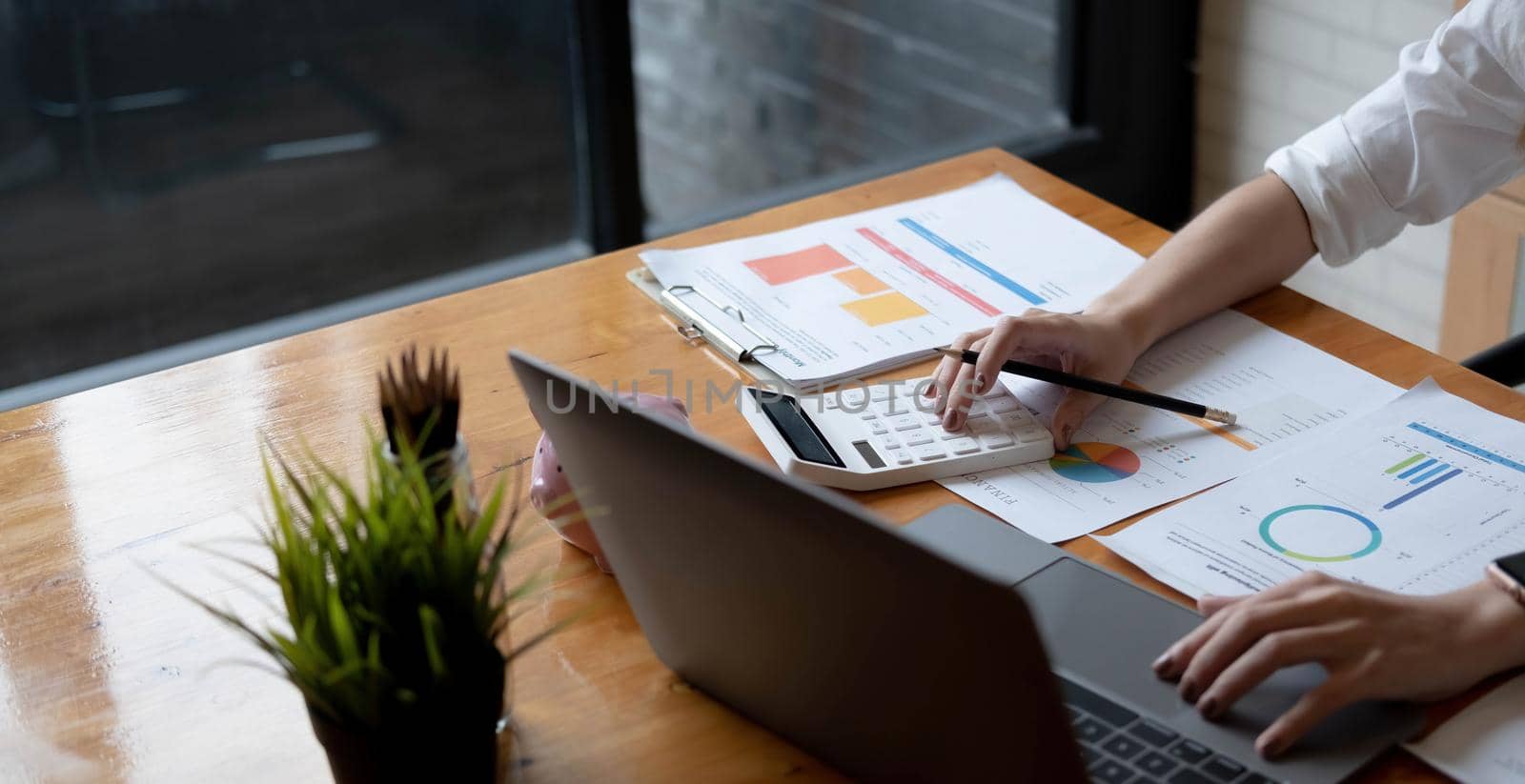 Close up Business woman using calculator and laptop for do math finance on wooden desk in office and business working background, tax, accounting, statistics and analytic research concept.