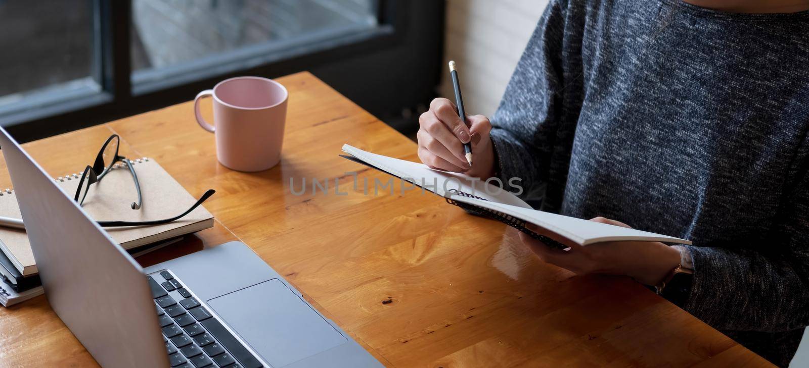 Cropped photo hand of woman writing making list taking notes in notepad working or learning online with laptop at home.