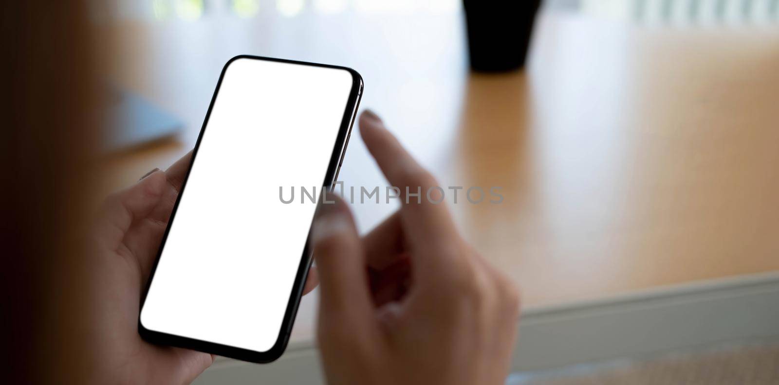 Mockup image blank white screen cell phone.women hand holding texting using mobile on desk at home office...