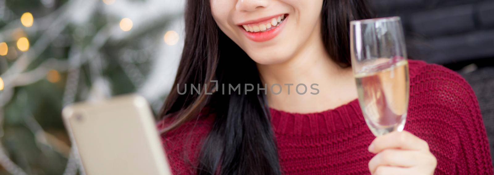 Young asian woman selfie video call online with friends and show glass in Christmas day on phone at home with social distancing, new normal, female video conference, communication and holiday concept. by nnudoo