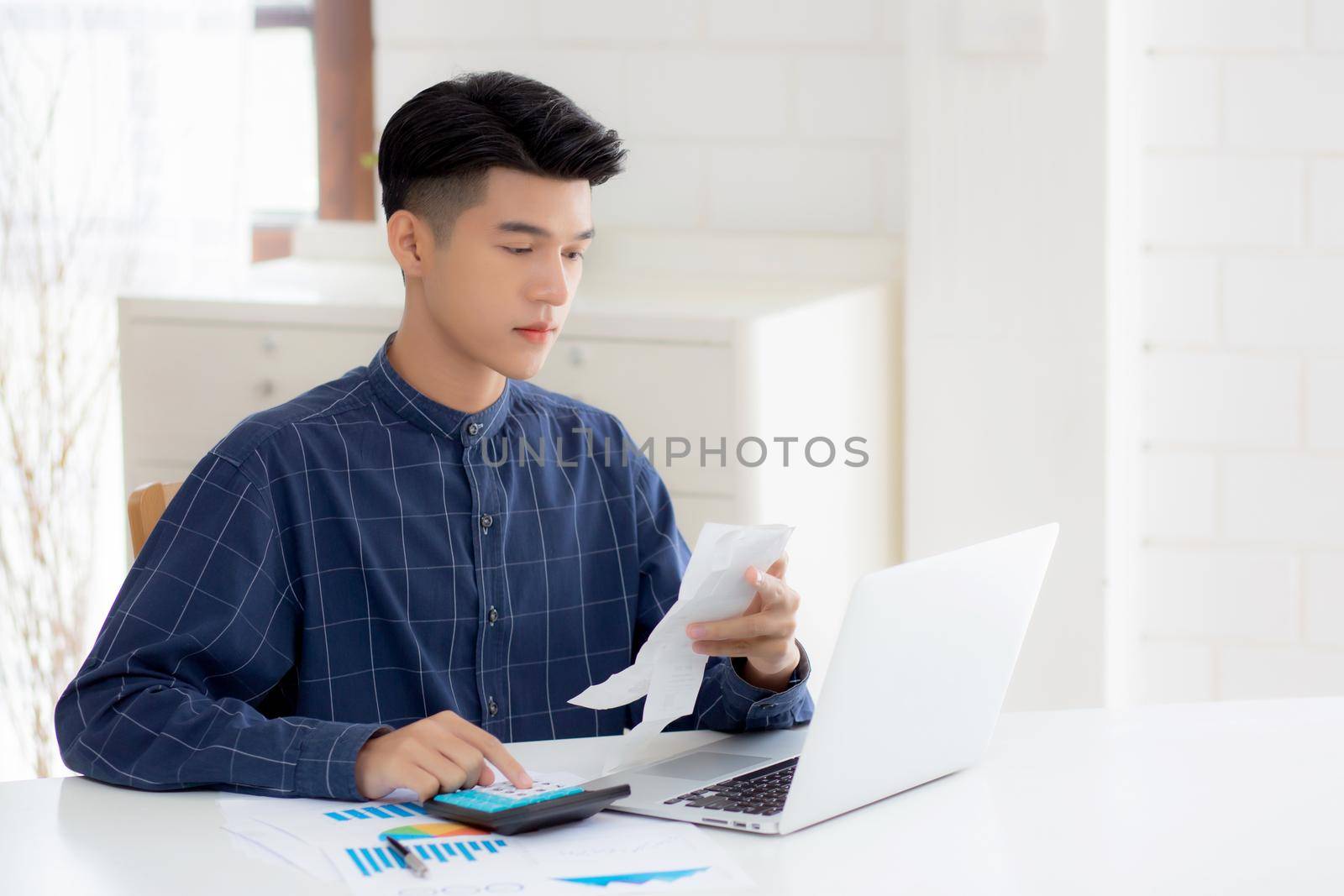Young asian man calculating finance household with calculator on desk at home, male checking bill and success for saving expenses household, debt closure, tax and accounting, business concept. by nnudoo