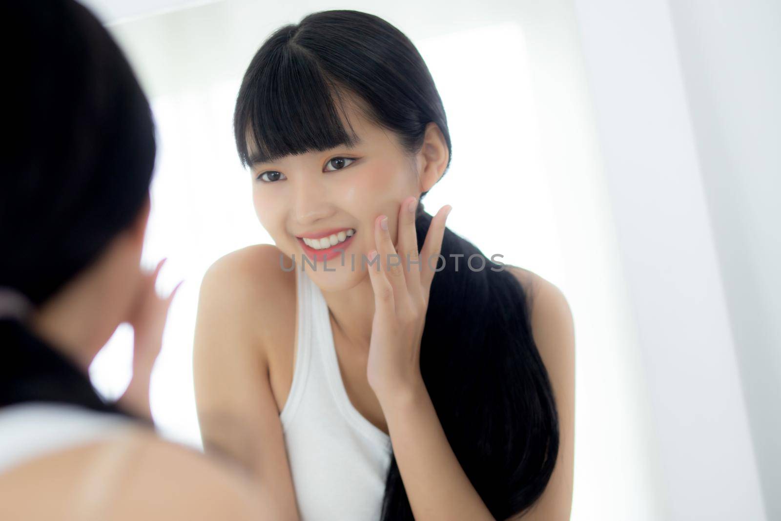 Beautiful face of young asian woman with happy smiling and touch cheek looking mirror with charming, makeup of beauty facial girl with skincare and cosmetic treatment, skin care and healthy concept. by nnudoo