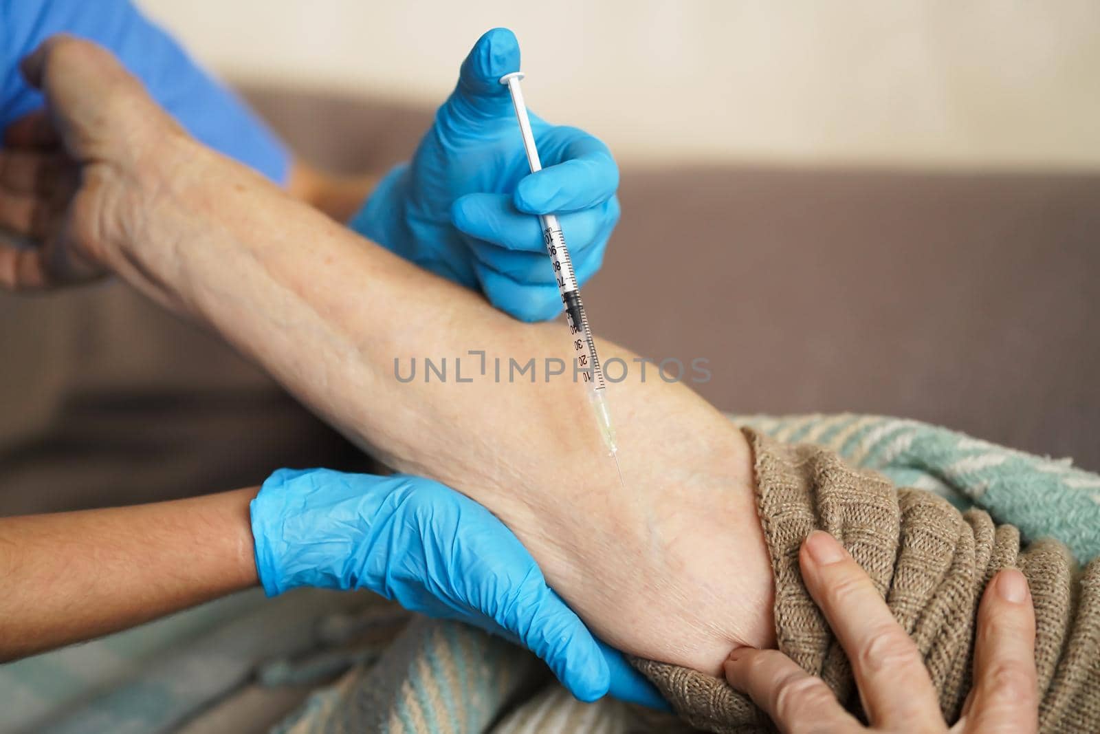 The nurse makes an injection with the vaccine to the patient at home. A young doctor in a blue suit holds the hand of an elderly woman and makes injection with a syringe. Medicine and healthcare.