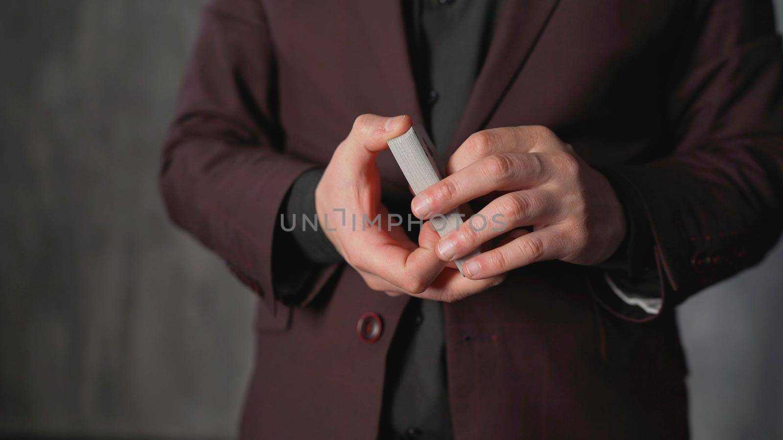 The magician tosses a playing card. Portrait of a young man with gambling. Dexterous hands of a magician on a brown texture. The concept of entertainment and hobbies.