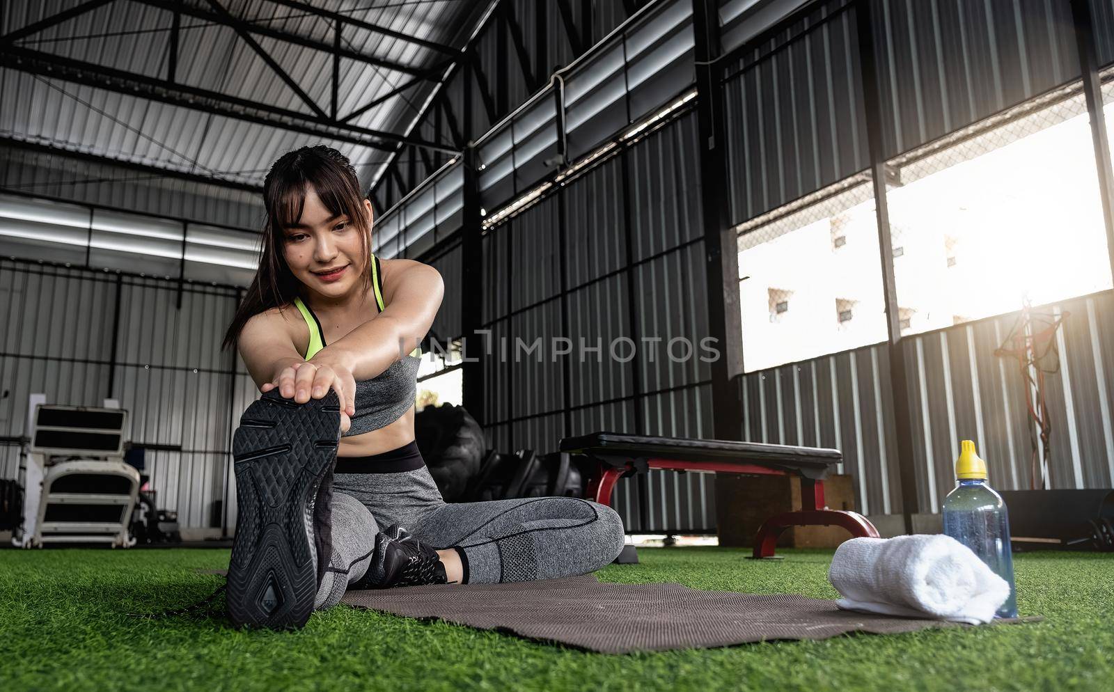 Young asian female in stylish and comfy sportswear stretching her legs on the fitness floor. exercise and sport concept. Fit woman doing stretching workout at gym.