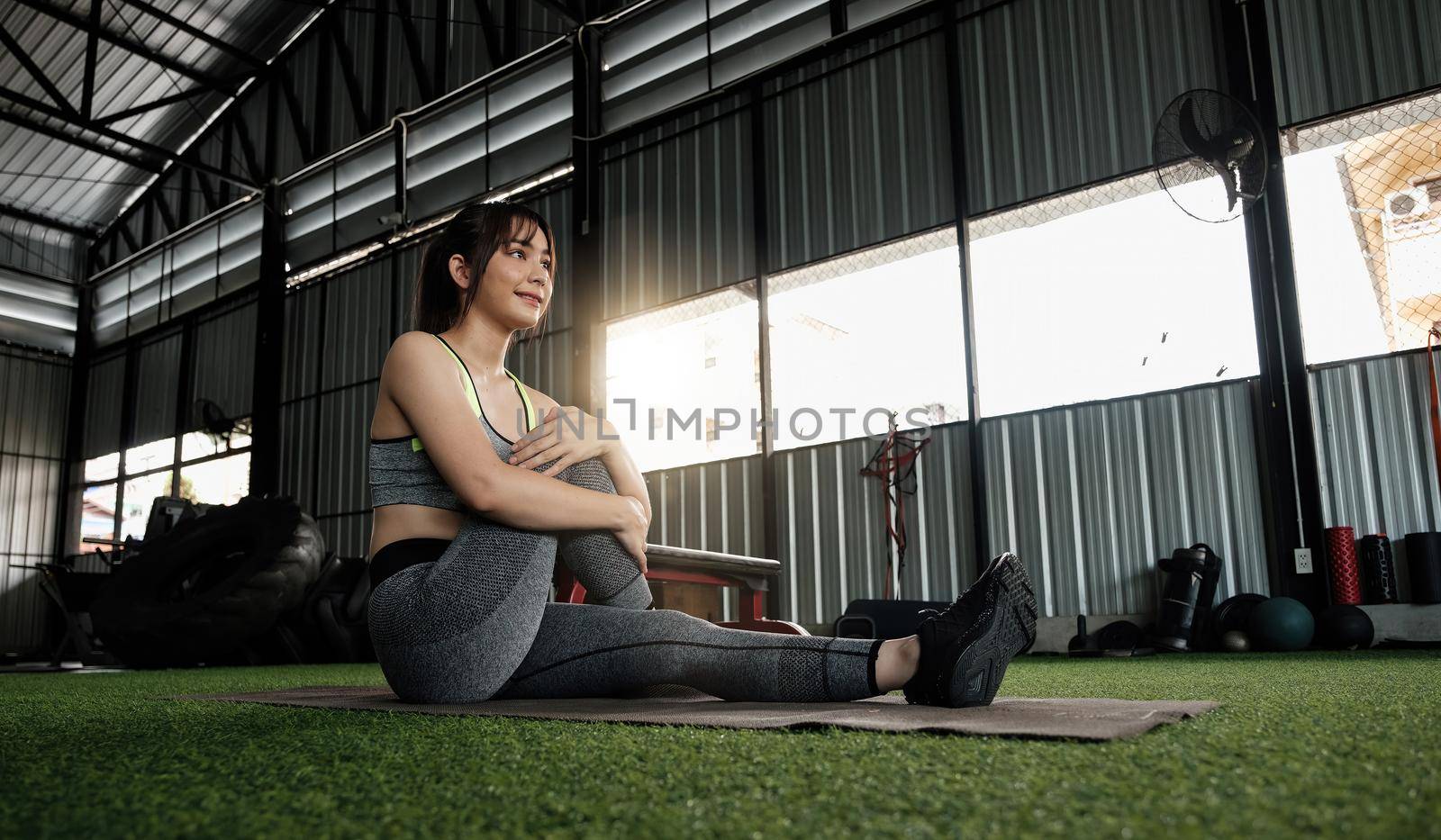 Young asian female in stylish and comfy sportswear stretching her legs on the fitness floor. exercise and sport concept. Fit woman doing stretching workout at gym.