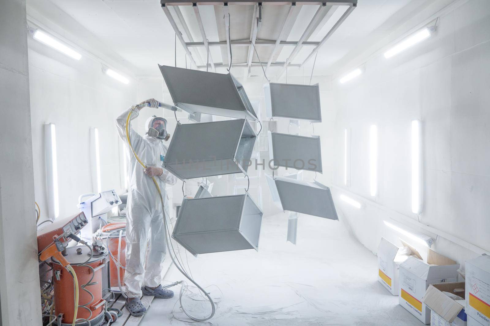 KYIV, UKRAINE - August 16, 2021: Powder coating of metal products in spray booth. Industry painting metal parts in paint booth. Coveralls worker with spray gun painting steel parts in painting chamber