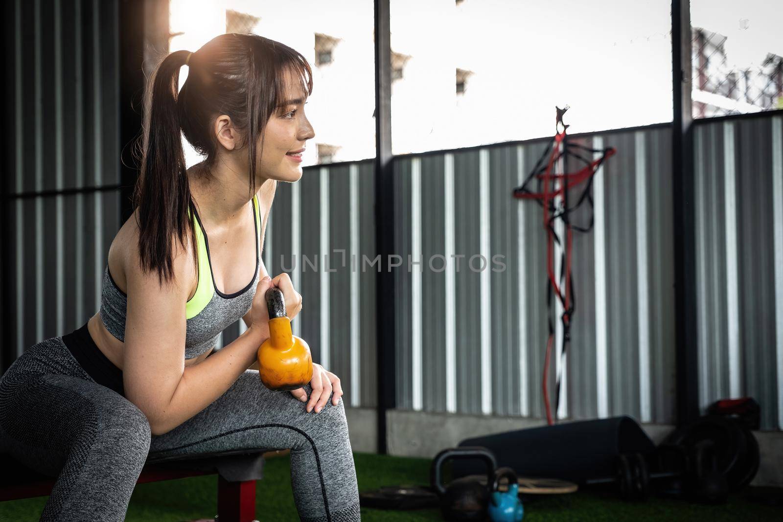 Young asian female enjoy exercising with lifting kettle bell with one hand at the gym. sport bodybuilding concept