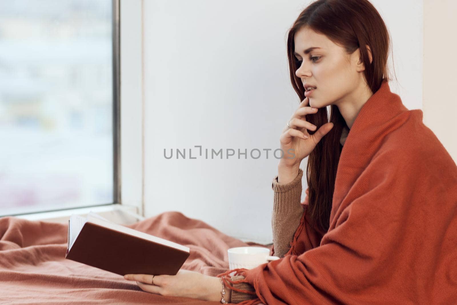 woman near the window with a plaid reading a book rest. High quality photo