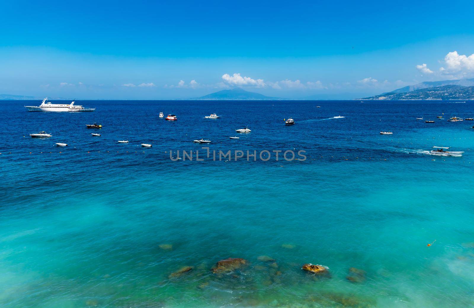 Blue azure coast next to small beach at Capri island with few boats on the sea