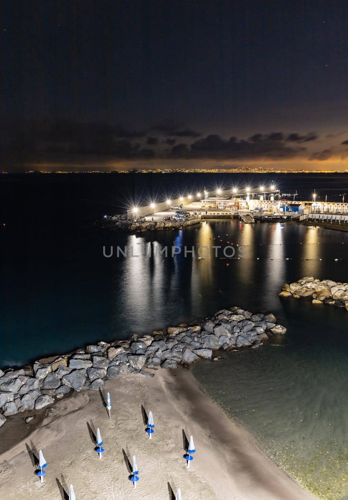 Night landscape of coast with small beach and breakwater with small pier by Wierzchu