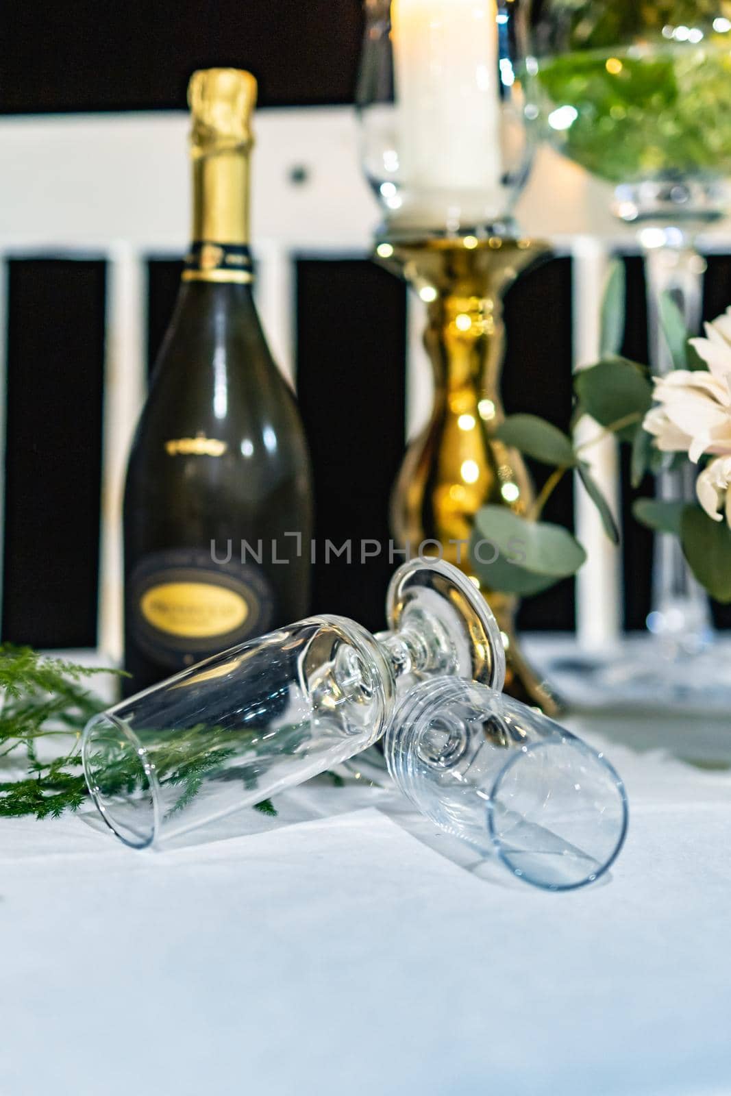 Two high champagne glasses lay on table in front of bottle of champagne and high glass candlestick