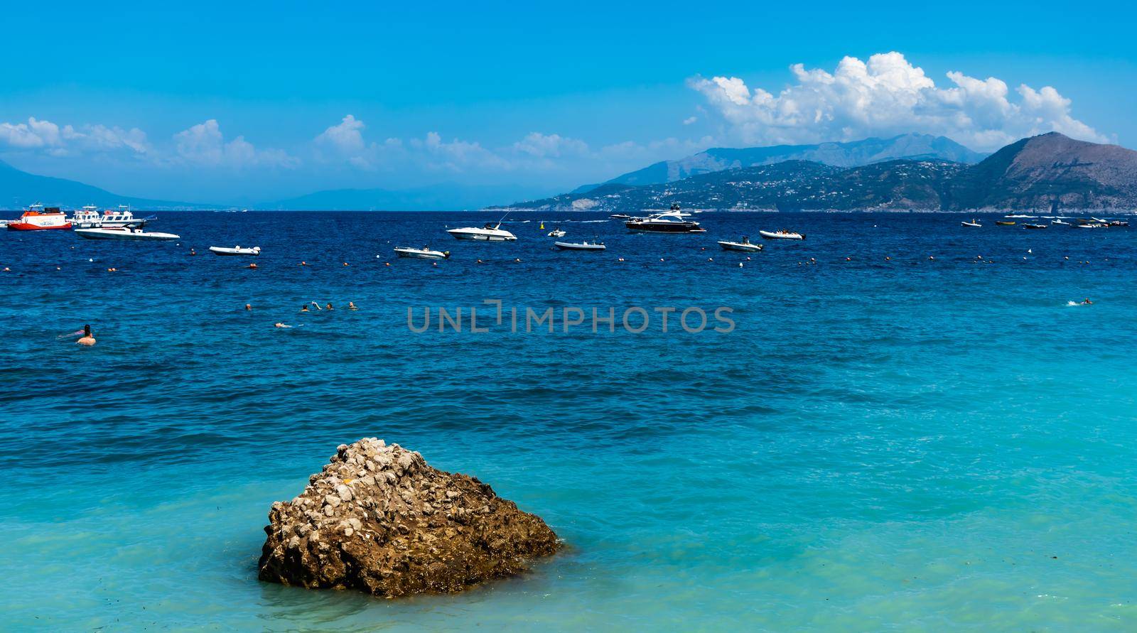 Blue azure coast next to small beach at Capri island with few boats on the sea by Wierzchu