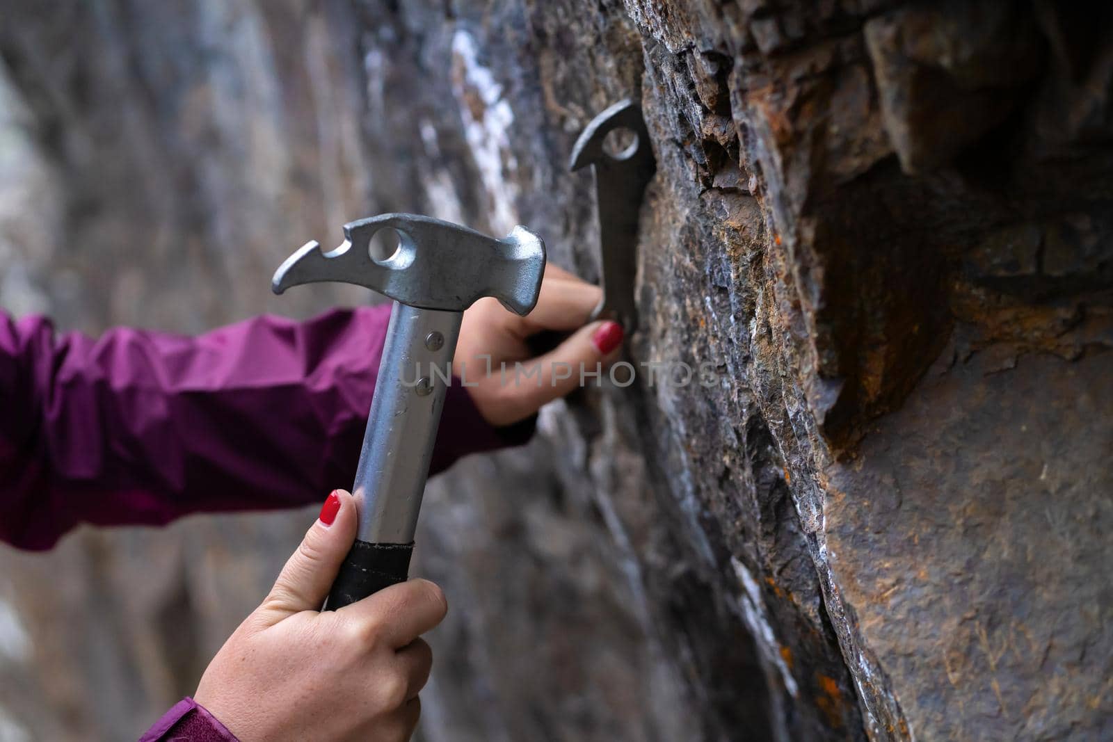 Women's hands hold a climbing hammer and drive the anchor into the rock, the climber makes a belay point on the route to the top of the mountain.