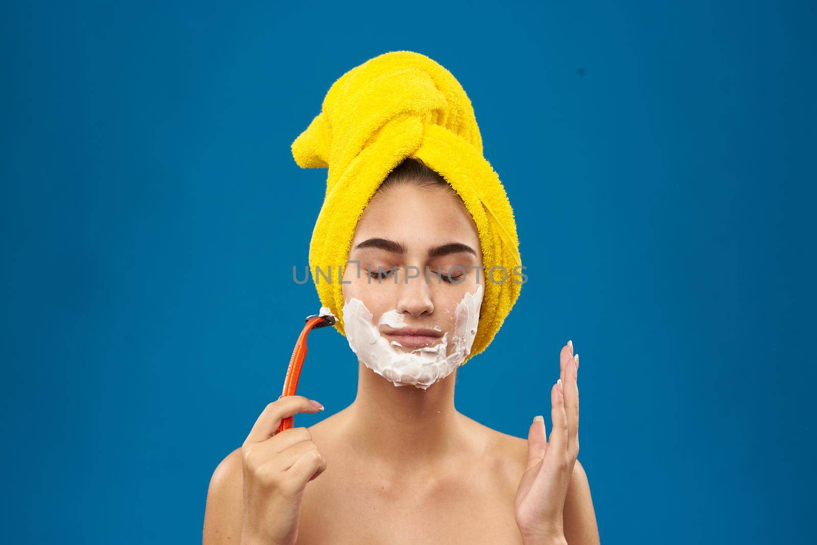 pretty woman with a yellow towel on his head shaving blue background. High quality photo