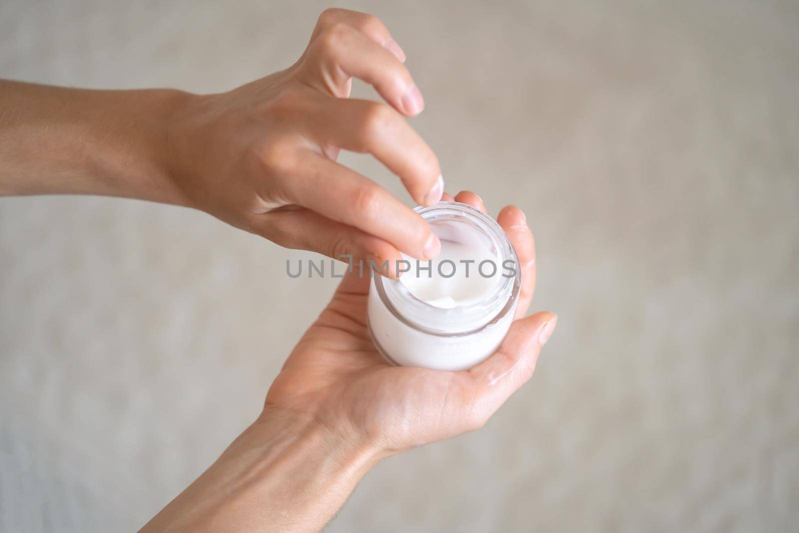 Young female hands hold a jar of moisturizing cream to maintain health, softness of the skin, the woman takes care of her health and beauty.