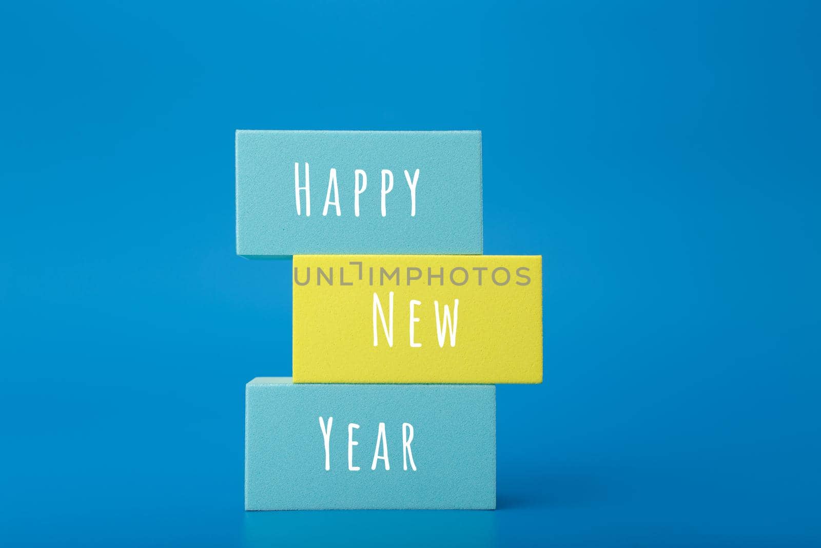 Happy New Year minimal trendy concept. Modern festive composition with stack of multicolored rectangles with written Happy New Year text against blue background 
