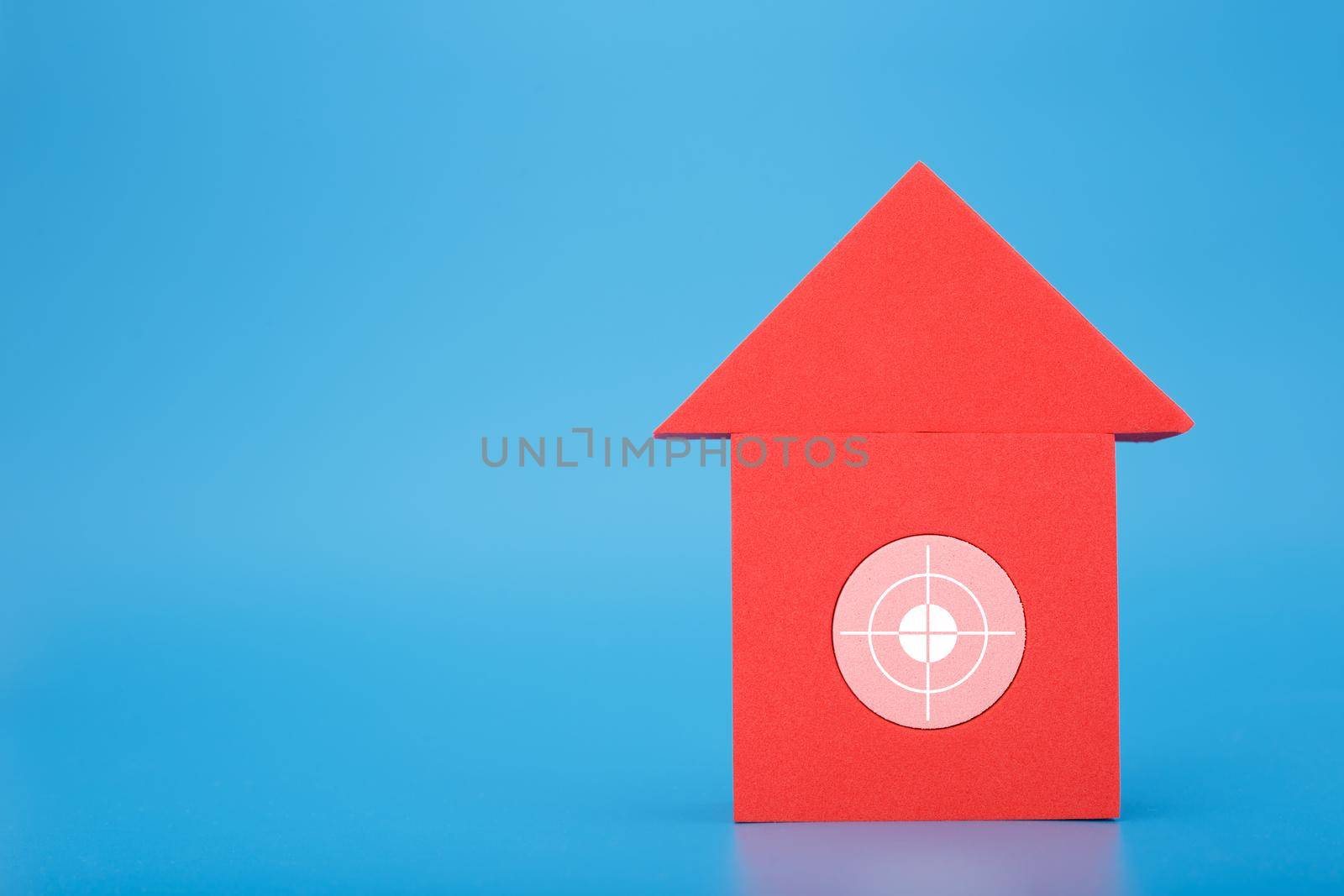 Red toy house with target in the middle against blue background with copy space. Concept of real estate, loan or mortgage by Senorina_Irina