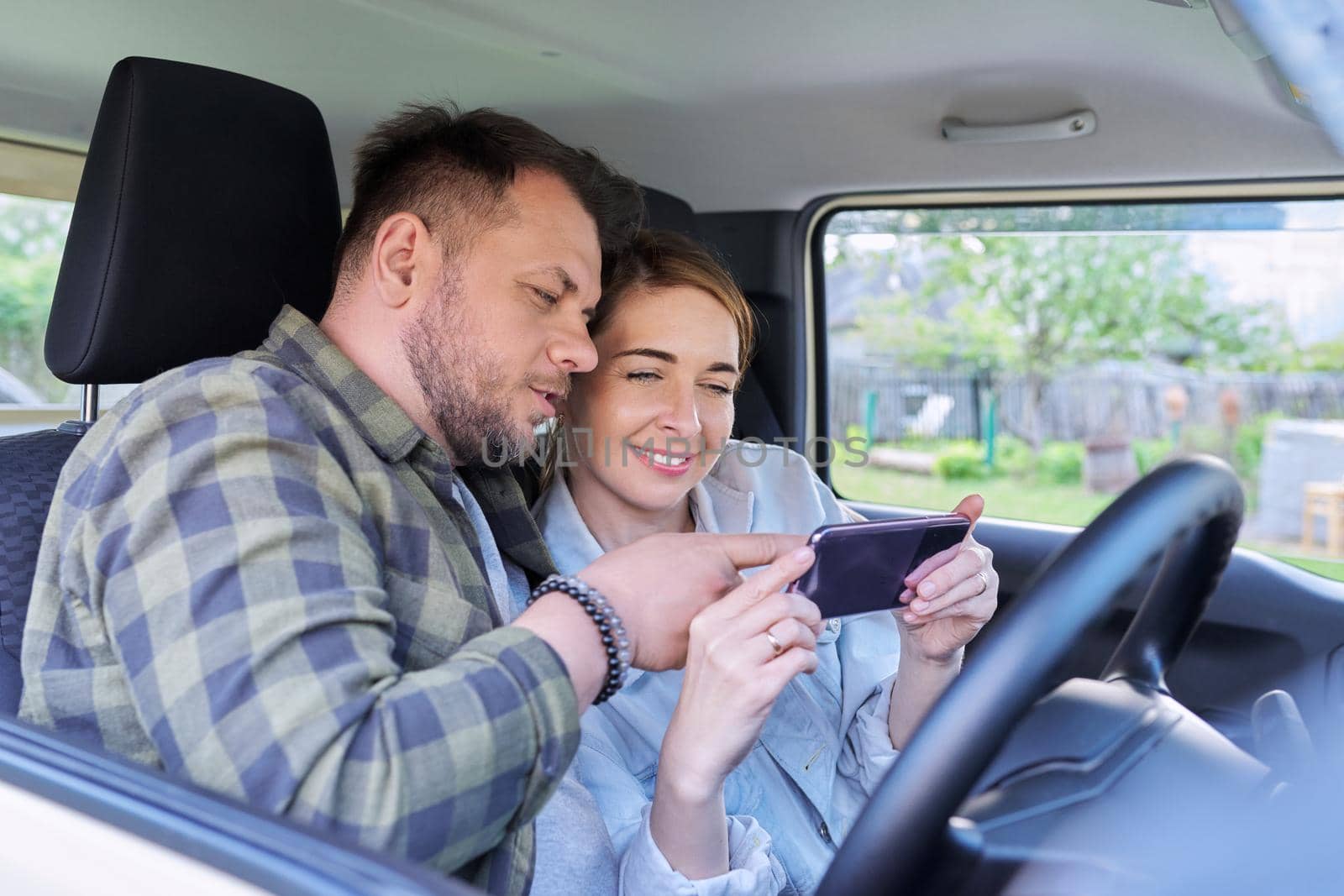 Happy middle aged couple using smartphone together sitting in the car. Family, relationship, trip, transportation, lifestyle, people 40 age concept