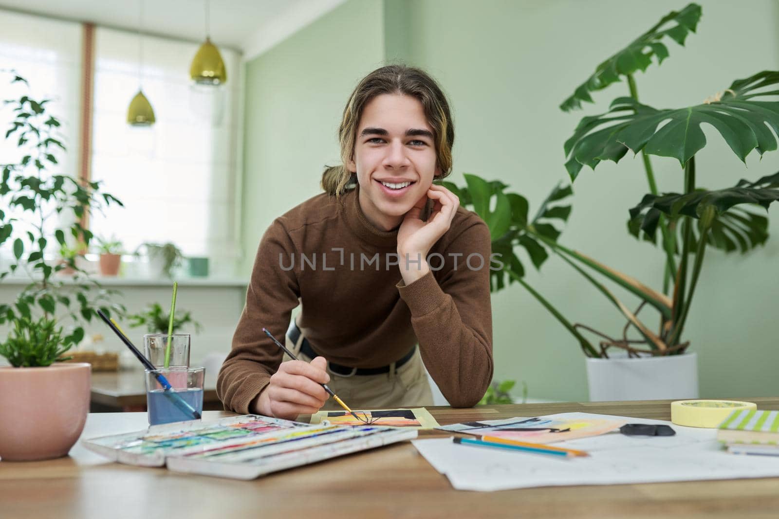 Teenager guy artist painting with watercolors at home. Portrait of a handsome teenage boy looking into the camera. Creativity, adolescence, hobbies and leisure