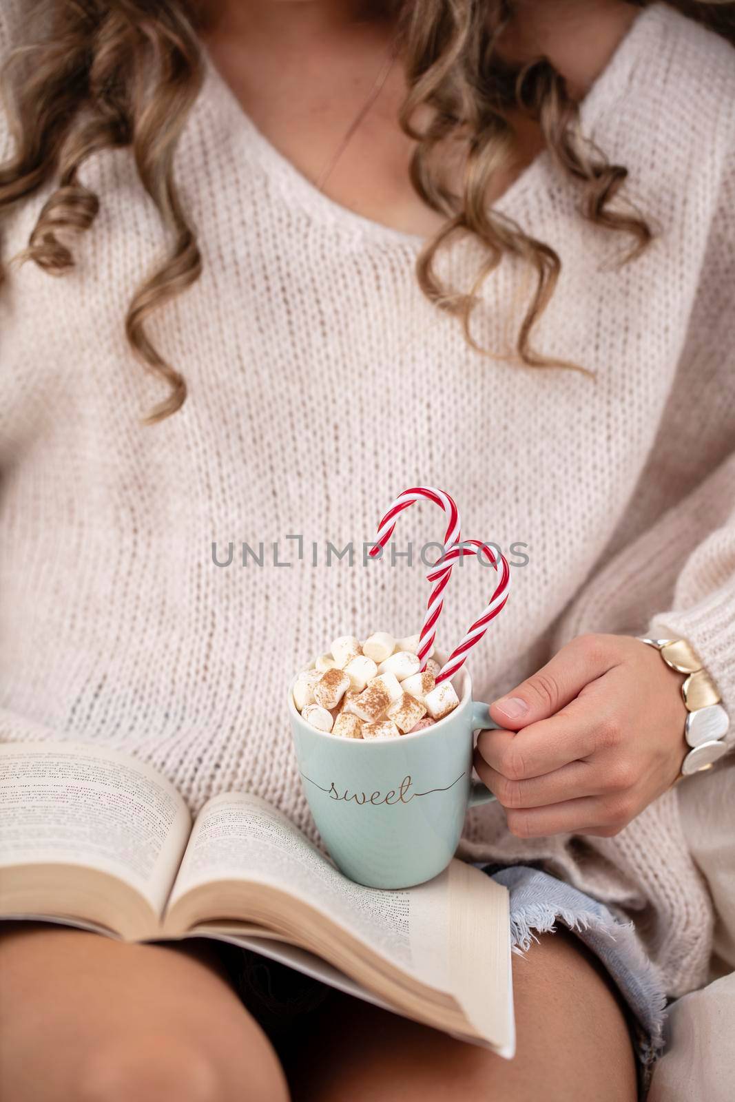 Girl in knitted wool sweater is holding a mug with hot chocolate with marshmallow. by gitusik