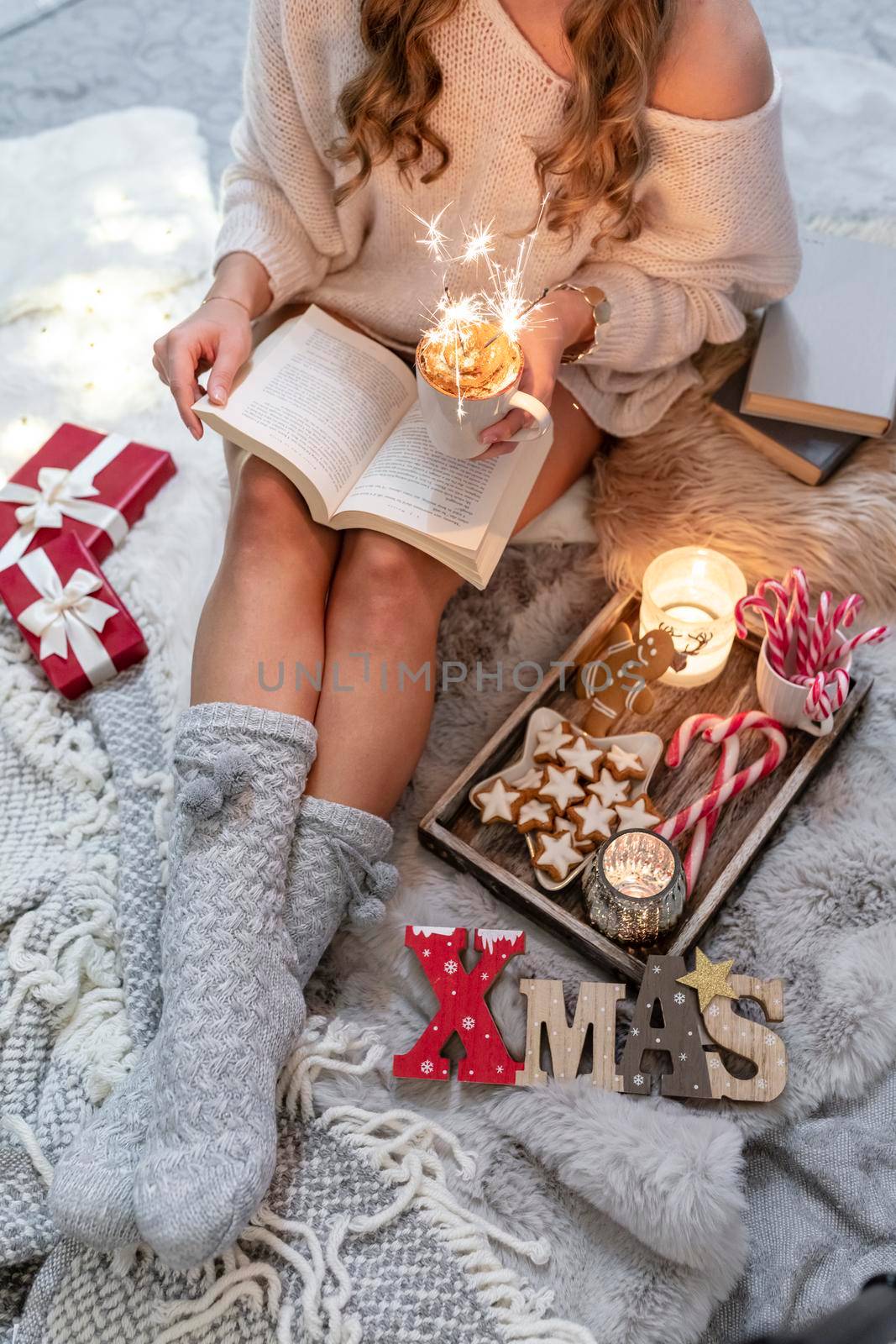 The girl is sitting in a christmas atmosphere, drinking a hot drink and reading a book.