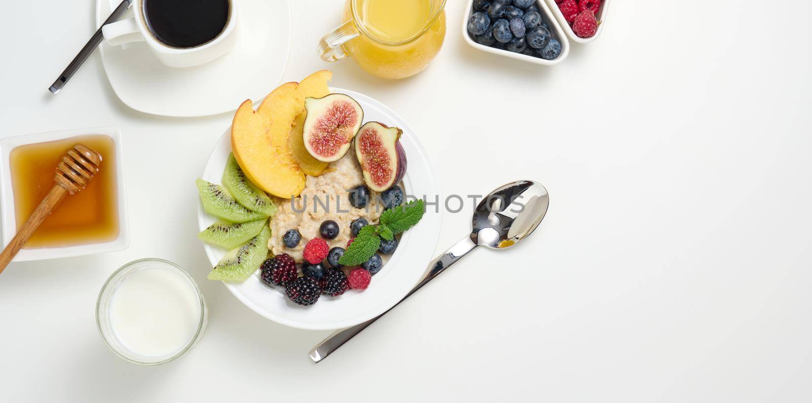 cup of black coffee, a plate of oatmeal and fruit, honey and a glass of milk on a white table, a healthy morning breakfast, top view by ndanko