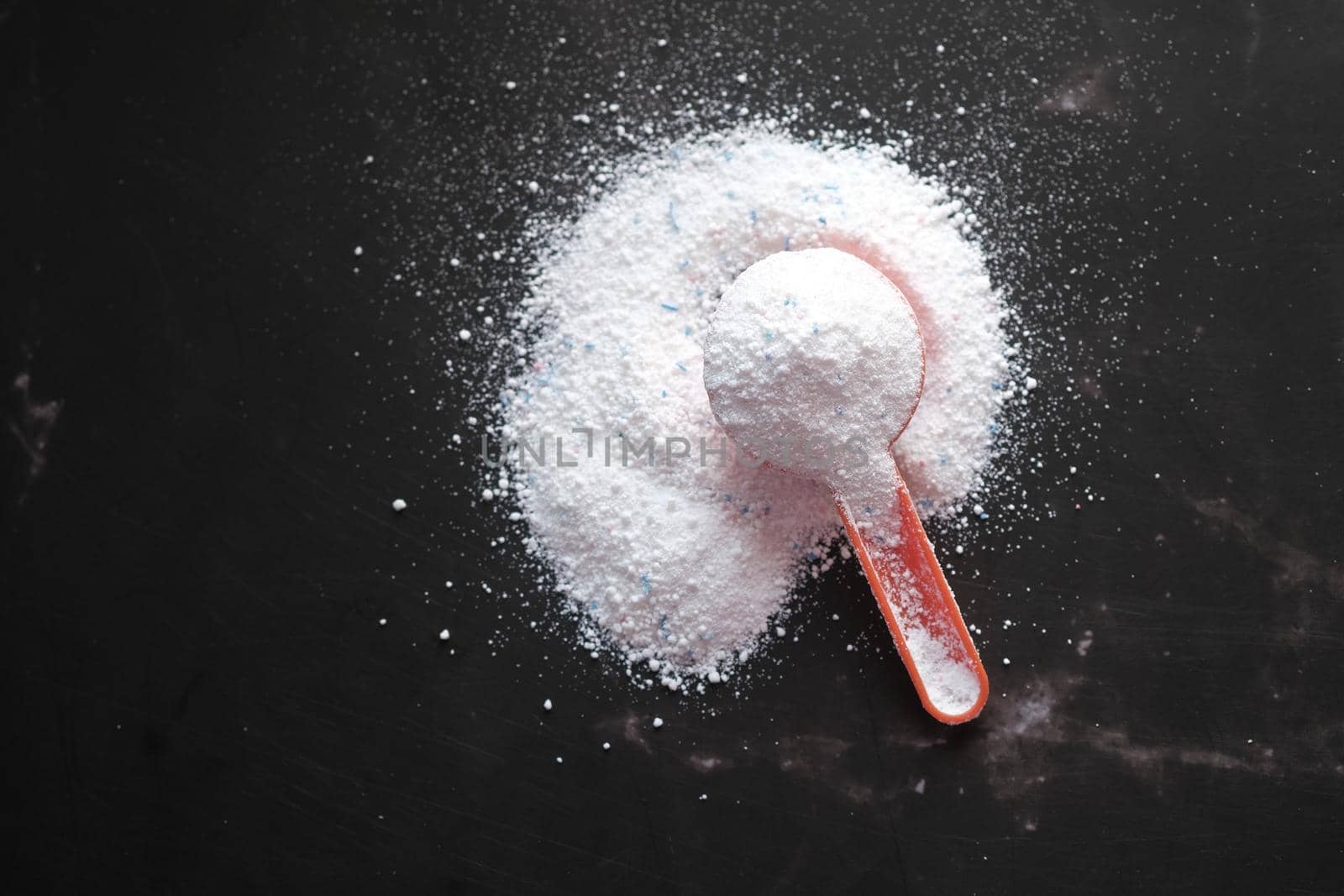 Washing powder in plastic spoon on black background top view