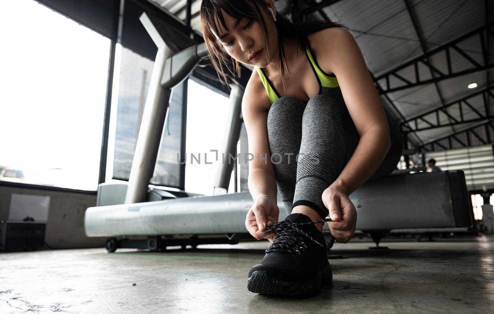 Close up of young asian woman lacing sports shoes before exercise at the gym. by nateemee
