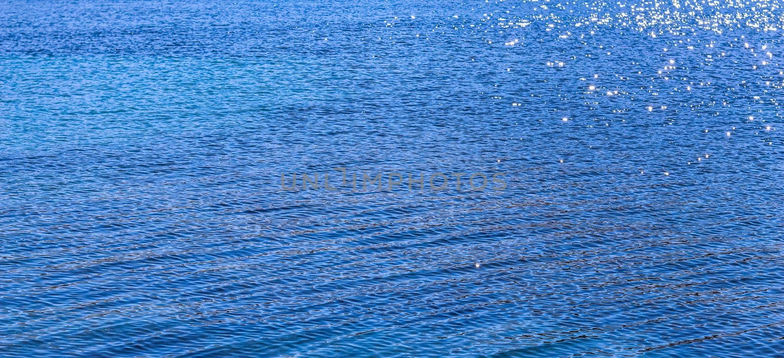 Blue sea in sunshine glow as surface background. Summer holidays and coastal nature concept