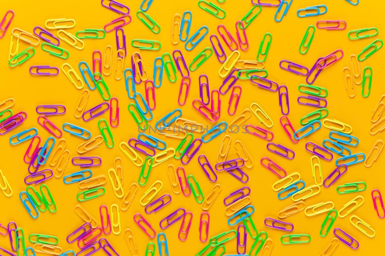 Color paper clips on yellow background, copy space. Top view, flat lay. Back to school, college, education concept. Collection of colorful paperclips. Abstract background.