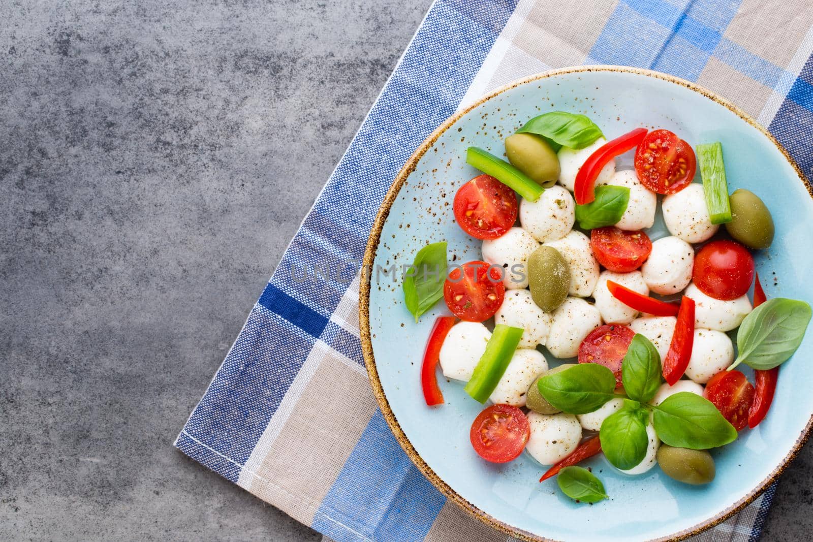 Cherry tomatoes, mozzarella cheese, basil and spices on gray slate stone chalkboard. Italian traditional caprese salad ingredients. Mediterranean food. 