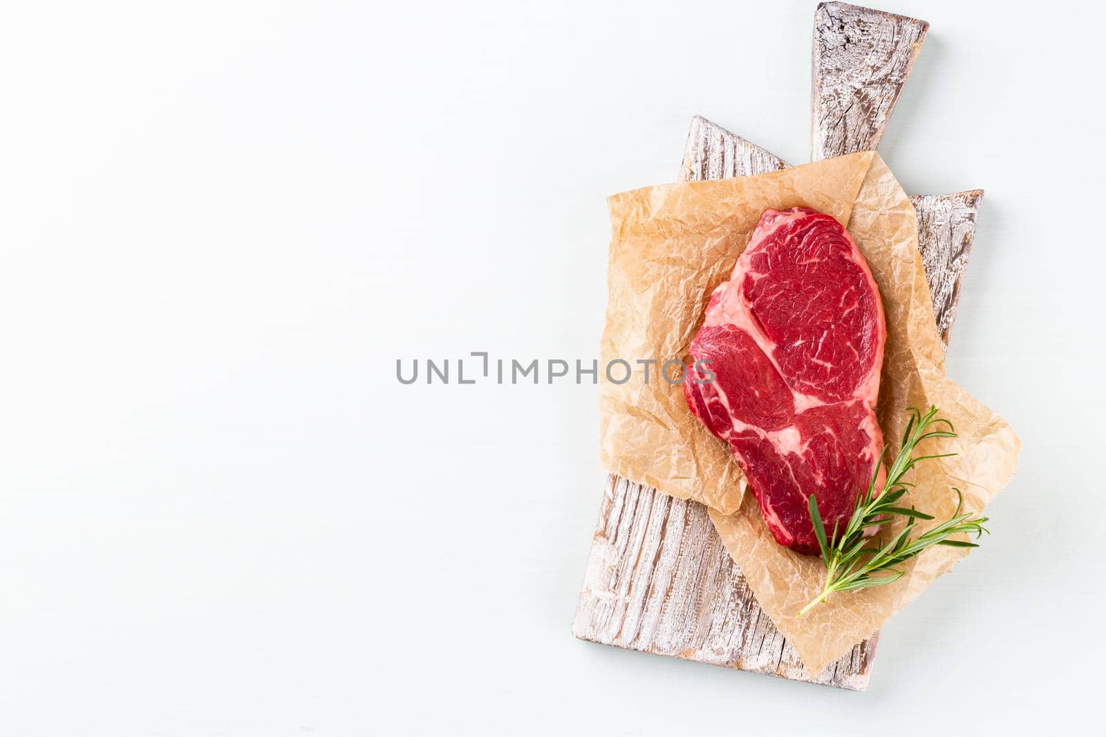 Fresh raw rib-eye steak on wooden cutting board, with spinach, lentils and rosmary in a rustic style.