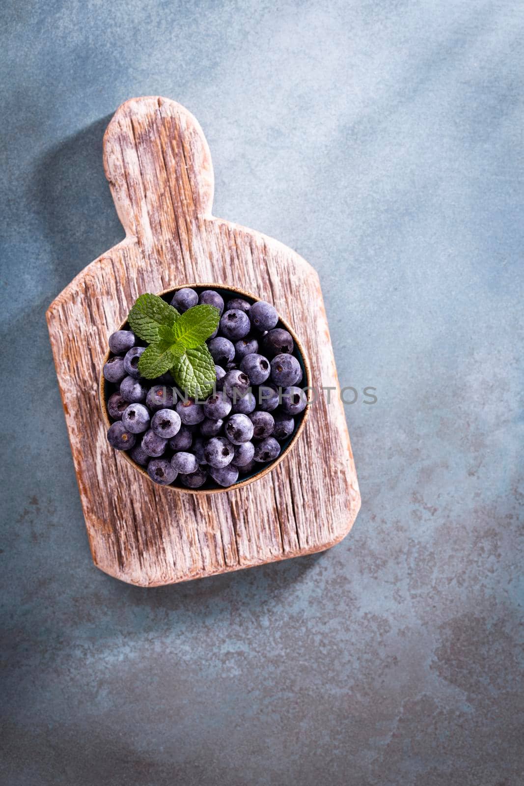 Bowl of fresh blueberries on rustic wooden board. Organic food blueberries and mint leaf for healthy lifestyle. by gitusik