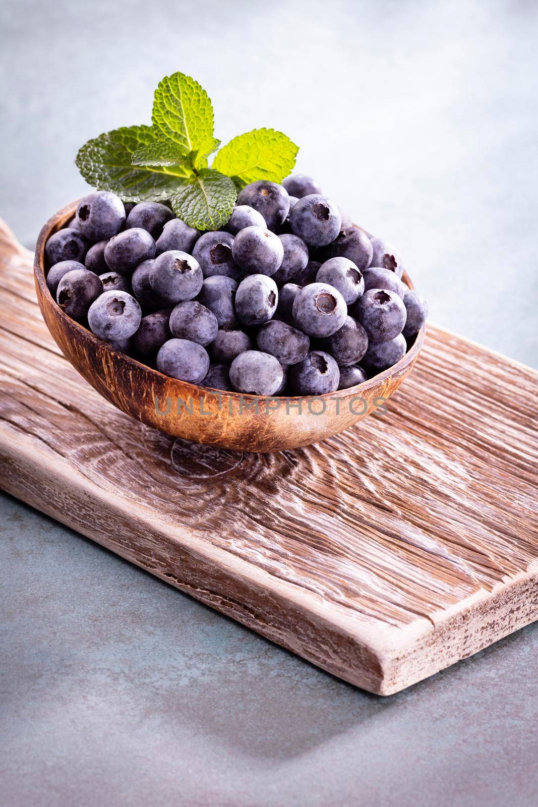 Bowl of fresh blueberries on rustic wooden board. Organic food blueberries and mint leaf for healthy lifestyle. by gitusik