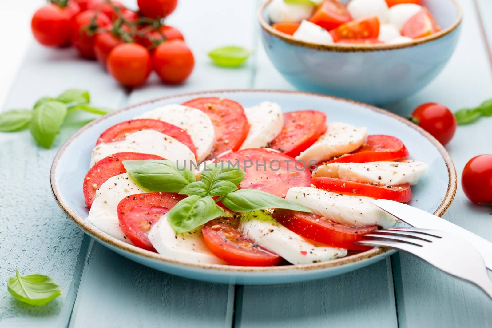 Tomatoes, mozzarella cheese, basil and spices on gray slate stone chalkboard. Italian traditional caprese salad ingredients. Mediterranean food.