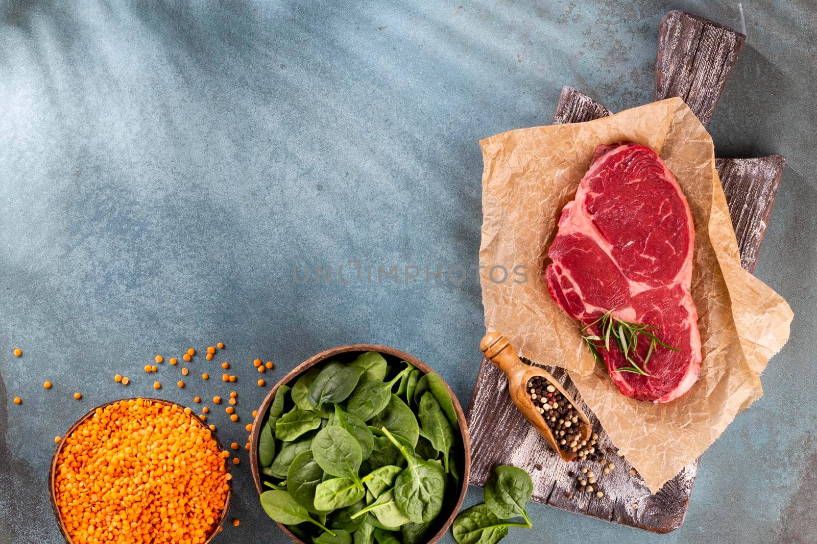 Fresh raw rib-eye steak on wooden cutting board, with spinach, lentils and rosmary in a rustic style.