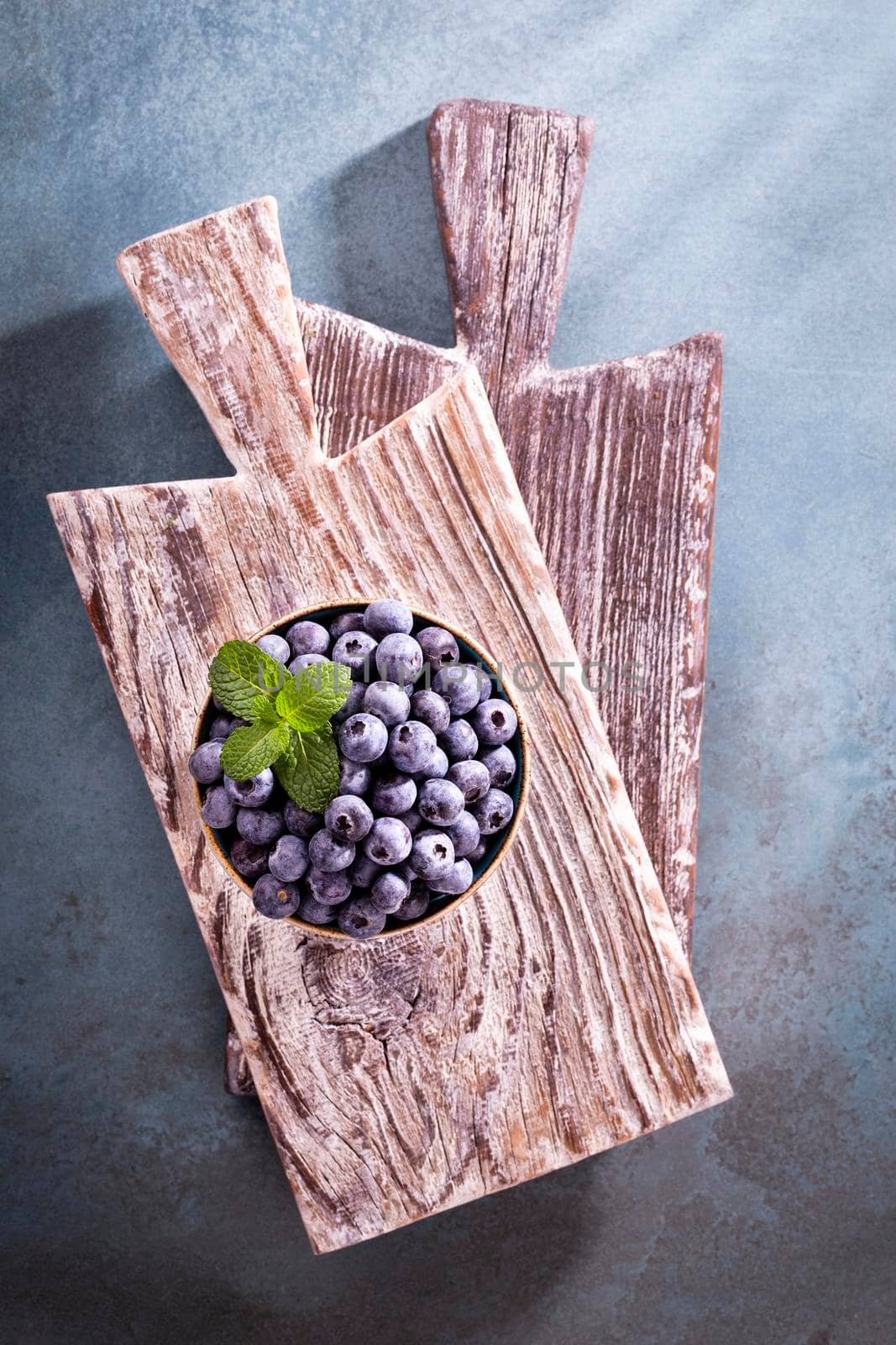 Bowl of fresh blueberries on rustic wooden board. Organic food blueberries and mint leaf for healthy lifestyle. by gitusik