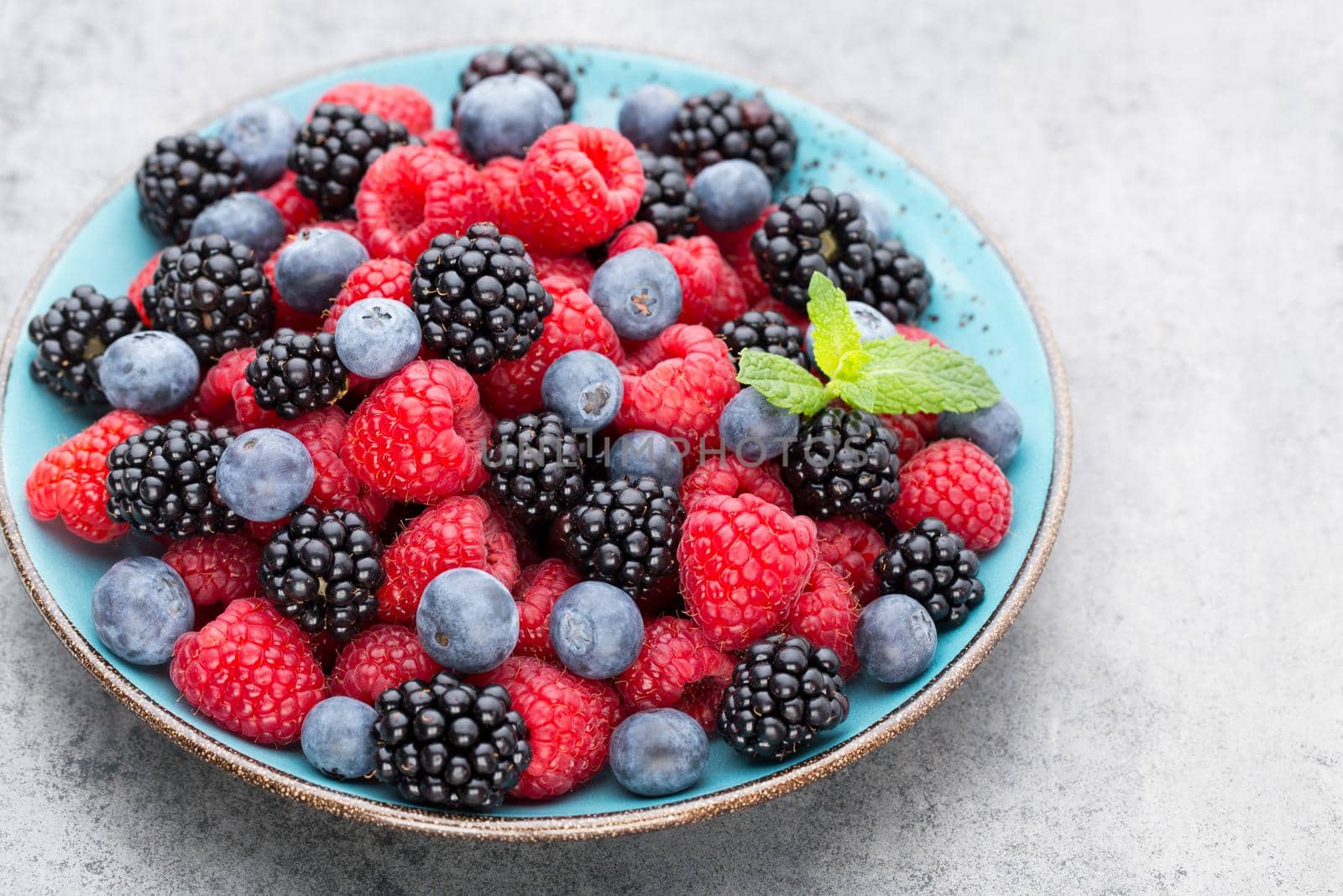 Fresh berries in a plate on a  wooden background. Flat lay, top view, copy space.