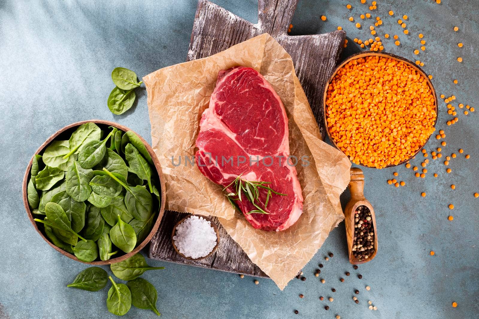 Fresh raw rib-eye steak on wooden cutting board, with spinach, lentils and rosmary in a rustic style.