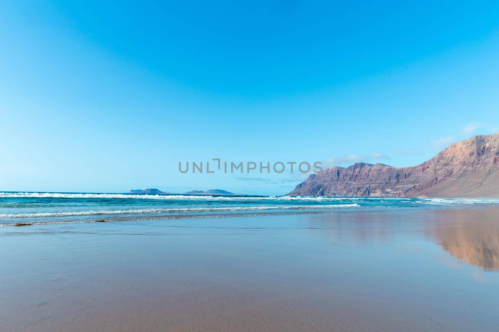 Panorama of beautiful beach and tropical sea of Lanzarote. Canaries. Coast of Famara beach, Lanzarote Island, Canary Islands. Tourists on the most popular beach at the island of Lanzarote.