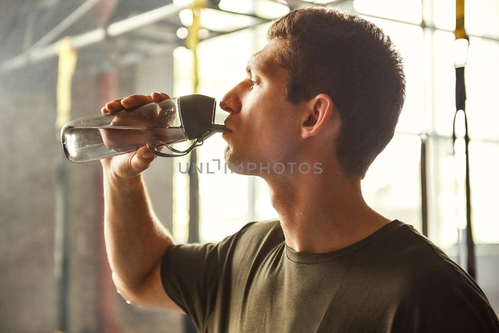 So thirsty. Young athletic man drinking water while exercising at gym by friendsstock