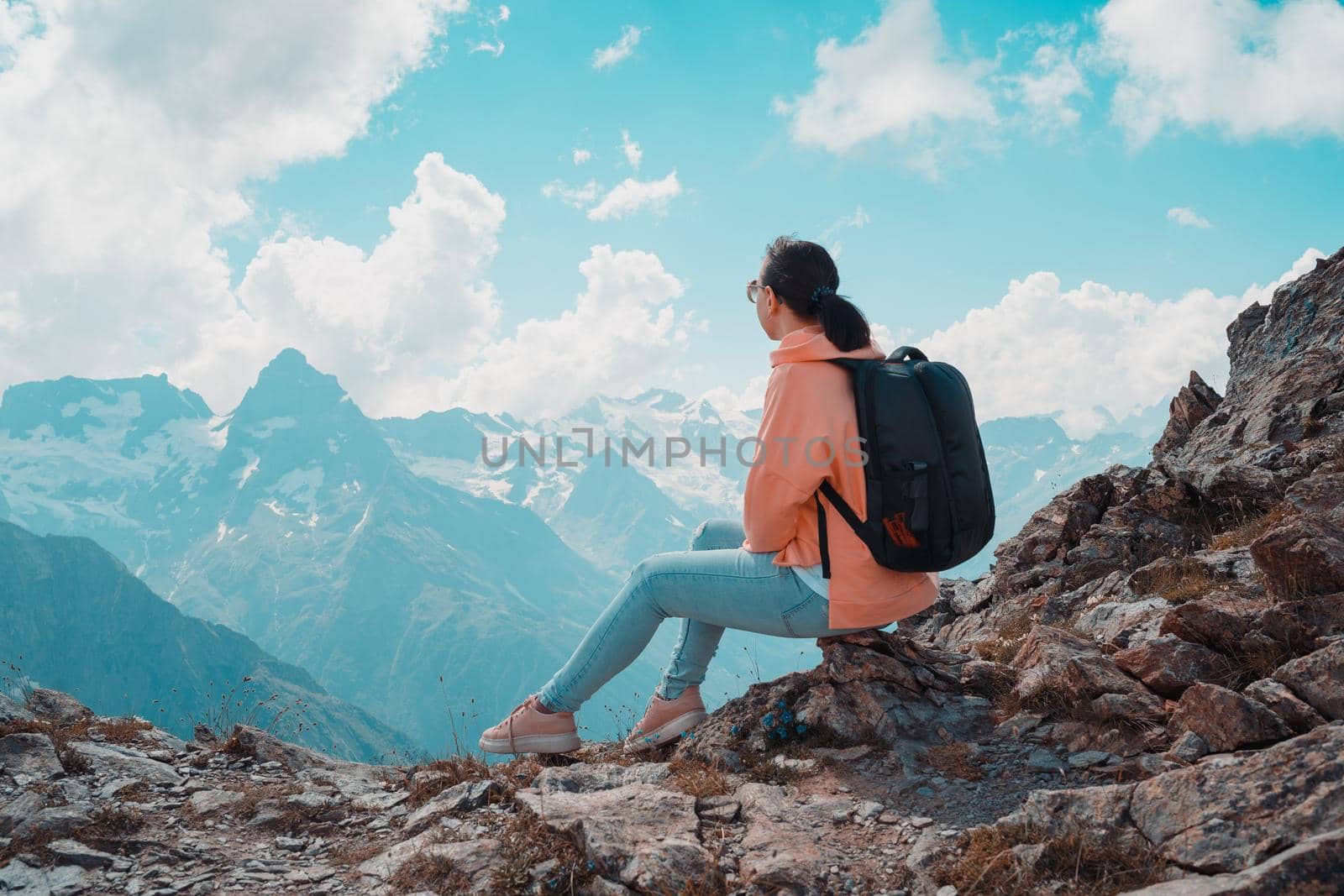 Young woman sitting on rock and looking at mountain landscape. Female traveler enjoying beautiful view in mountainous area. by epidemiks