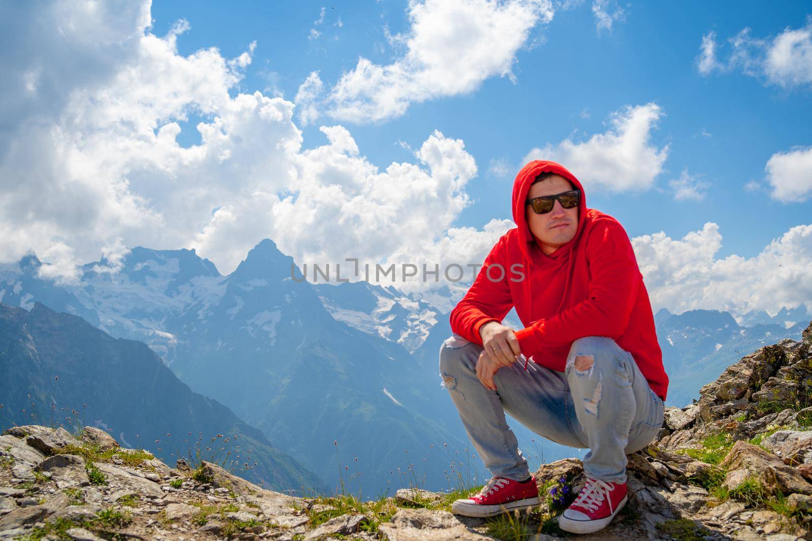 Adult male in red hoodie with hood enjoying beautiful view in mountainous area.