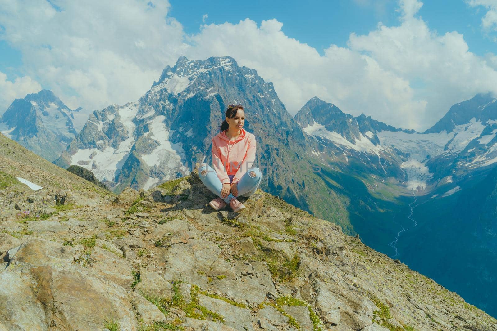 Young woman sitting on rock and looking at mountain landscape. Female traveler enjoying beautiful view in mountainous area. by epidemiks