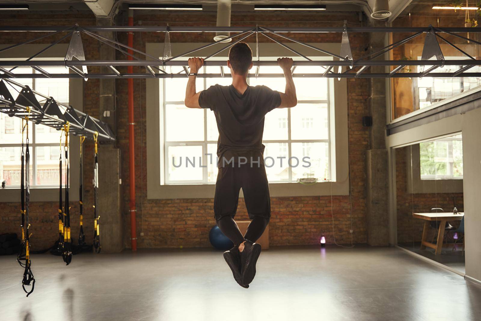 Never give up Back view of strong man doing pull-ups while exercising in the gym by friendsstock
